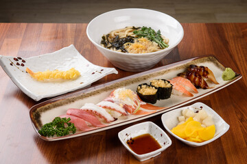 Traditional Japanese meal set with udon noodles, assorted nigiri sushi and fresh garnish on a wooden table