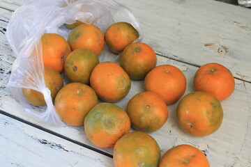 A bunch of oranges in a plastic bag on a wooden table

