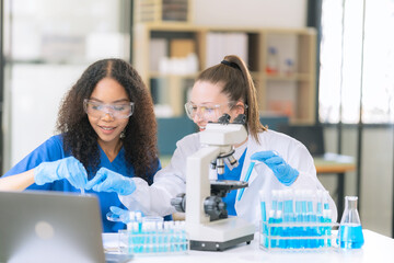 Two female scientists examine liquids in test tubes in a modern laboratory, handling chemicals and...
