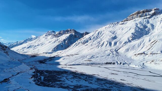 Aerial drone shot highlighting the frozen beauty of Spiti&rsquo;s mountains and river, as sunlight glistens over the ice and snow-covered slopes.