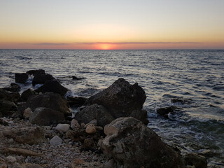 view of the sunset in the sea from a rocky rocky wild beach in summer
