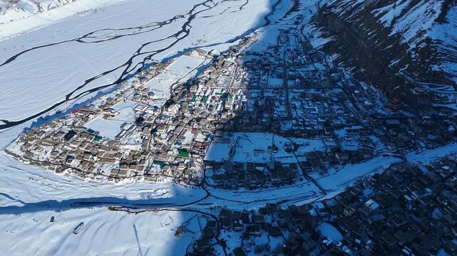 Aerial drone shot displaying the serene beauty of Kaza, where the warm sunlight gently melts patches of snow, revealing the rugged terrain beneath.