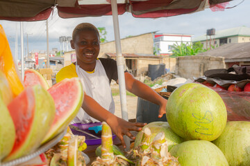 Happy African fruit seller standing behind watermelon conducting her business