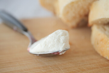 Fresh spread of creamy cheese on a spoon beside sliced bread