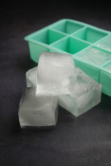 Ice cubes in various sizes beside a mint green ice tray