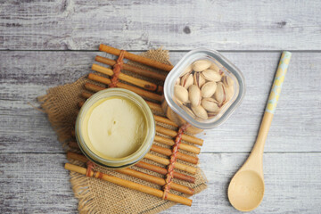 Creamy nut spread beside pistachios and wooden spoon on a table