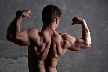 Muscular man flexing arms, back definition under dramatic lighting. Bodybuilding, fitness model