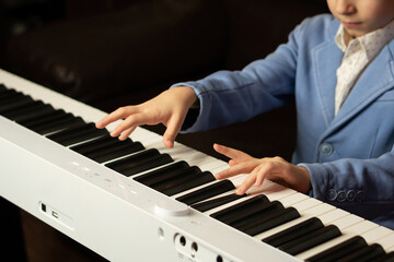 Obraz premium Close-up of a young boy's hands playing a white digital piano. Learn piano at home. The concept of education