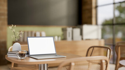The white screen laptop, books and a coffee on wooden table with the blurred background of cosy cafe