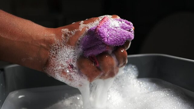 Hand washing a purple cloth in soapy water in the evening