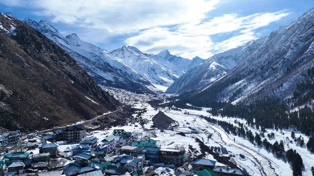 Aerial drone shot capturing the breathtaking beauty of Chitkul blanketed in snow, with its traditional wooden houses nestled in the white Himalayan landscape.