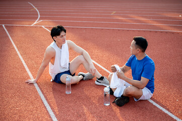 Two asian athlete men are taking a rest, sitting together on racetrack. Jogging or Running.