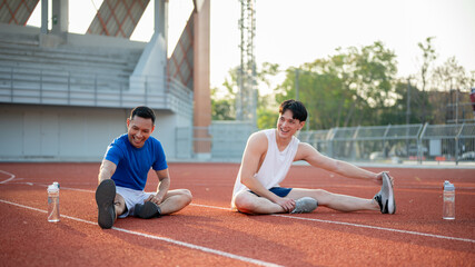 Two asian athlete men are happily stretching their muscles together on racetrack.Outdoor exercise.