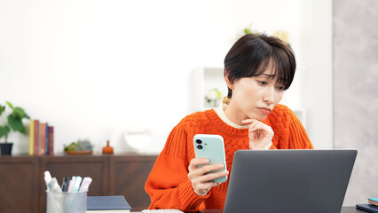 スマホとノートパソコンを見ながら悩むミドル女性