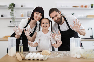Happy Caucasian family enjoying time together in modern kitchen cooking and playing with flour....