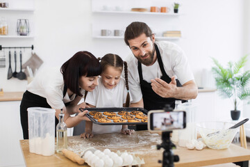 Caucasian family with male, female adults and child baking cookies in modern kitchen while...