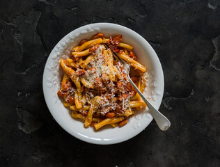 Quick and simple pasta with bacon and canned beans in tomato sauce on a dark background, top view