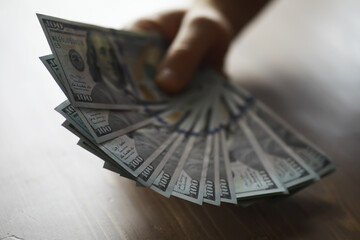 Hand Holding Fan of One Hundred Dollar Bills on Wooden Table