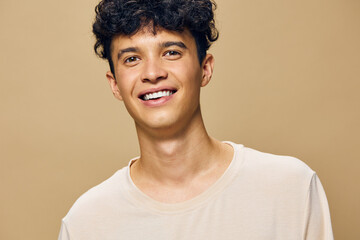 Smiling young man with curly hair wearing a light shirt, set against a warm, beige background that enhances the cheerful and friendly atmosphere of the portrait