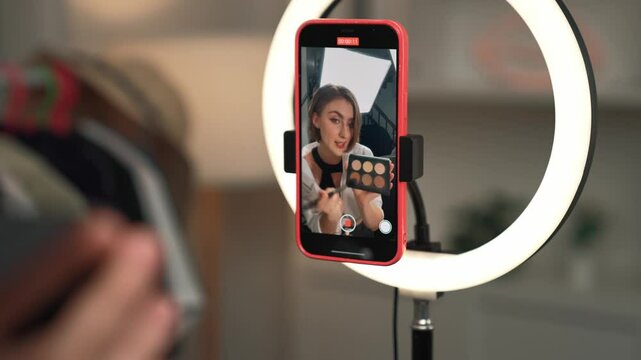 Back view influencer shoot live with smartphpone streaming using vlog video review makeup prim social media or blog. Girl with cosmetics studio lighting for marketing recording session online.