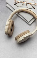 Modern wireless headphones lying on table next to books and eyeglasses