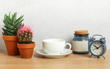 Coffee cup, alarm clock, and cacti creating relaxing morning atmosphere