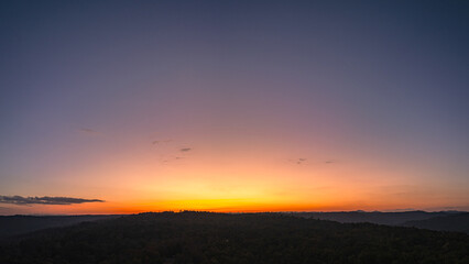 Aerial panorama view  A breathtaking sunset paints the sky with vibrant hues of orange and red, .casting a warm glow over the majestic mountains in a tranquil evening landscape.