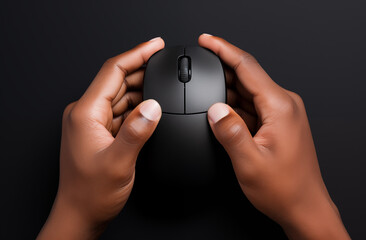 Hands holding a black computer mouse on a dark background in a close up studio shot from above  