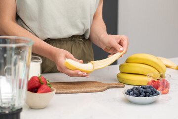 Preparing fresh banana smoothie with strawberries and blueberries on a kitchen counter