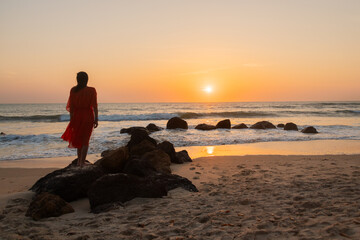 silhouette of a woman in red dress standing on rocks in the ocean on the beach at sunset