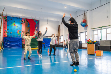 Students jumping and raising their arms, following their gym teacher's instructions during a...