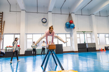 Young gymnast practicing split leap over pommel horse during physical education class, showcasing athleticism and balance in school environment