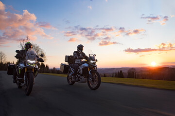 Fototapeta premium Drivers riding motorcycle on empty road during sunset, spring mountains