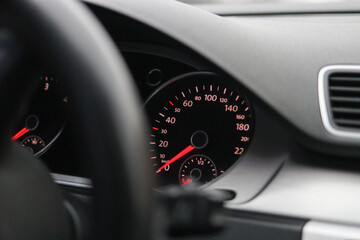 Close-up of a car dashboard showing speedometer and tachometer with red needles, taken from the...