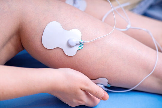woman attaches muscle stimulator electrodes to her leg for EMS training, showcasing modern fitness recovery technology