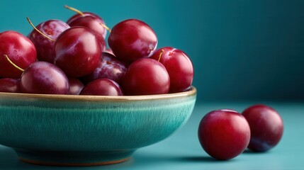 Fresh plums in turquoise ceramic bowl against teal background