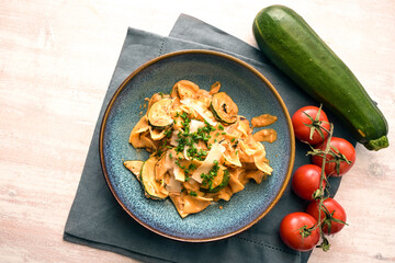 Tagliatelle pasta with zucchini in tomato sauce, parmesan cheese and chives garnish in a blue plate...