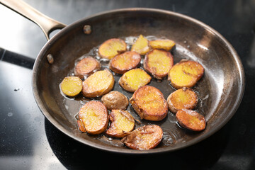 Crispy fried slices of potatoes with plenty of oil in a seasoned iron frying pan, rustic vegetarian meal, selected focus