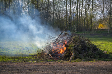 Large heap from branches, twigs and tree cuttings burning on a meadow, garden fire or traditional...
