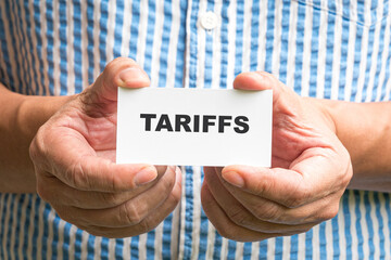 Man holding a white card with Tariffs message.