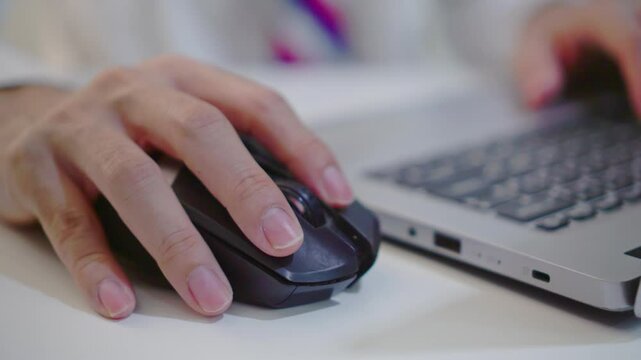 Close-up of freelancer's hand clicking a mouse in a coworking space. Businessman in white shirt and tie works on computer, copywriter editing or writing text while working from home or office setting.