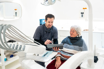 Dentist showing results on tablet to senior patient in modern clinic