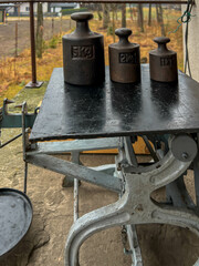 Old cast iron weights standing on a pine board, in the background a village and a sparse forest