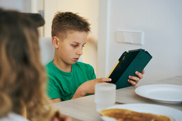 Boy using tablet at breakfast table with pancakes and water