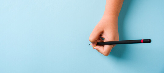 Left hand holding a ballpoint pen on an open notebook on a blue background