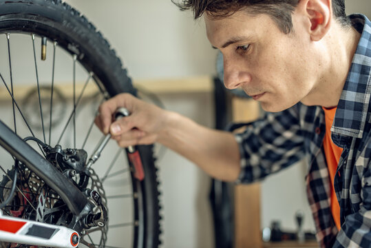 A male bicycle mechanic in the workshop disassembles a mountain bike and repairs it. Maintenance concept, preparation for the new season