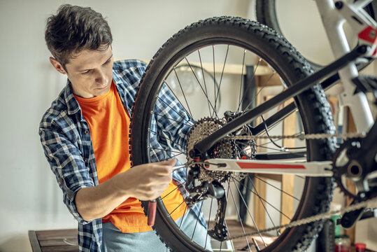 A male bicycle mechanic in the repair shop disassembles a mountain bike and repairs it. Maintenance concept, preparation for the new season - Powered by Adobe