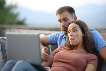 Confused couple watching media content on laptop in a terrace