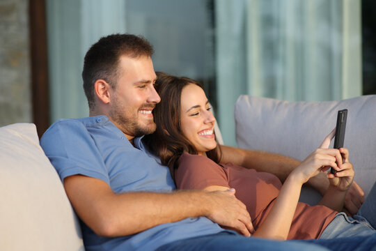 Happy couple in a terrace at home checking phone