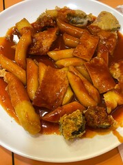 Spicy Korean tteokbokki with chewy rice cakes in a vibrant red sauce, topped with sesame seeds and green onions. A popular street food known for its addictive flavor and satisfying texture.
